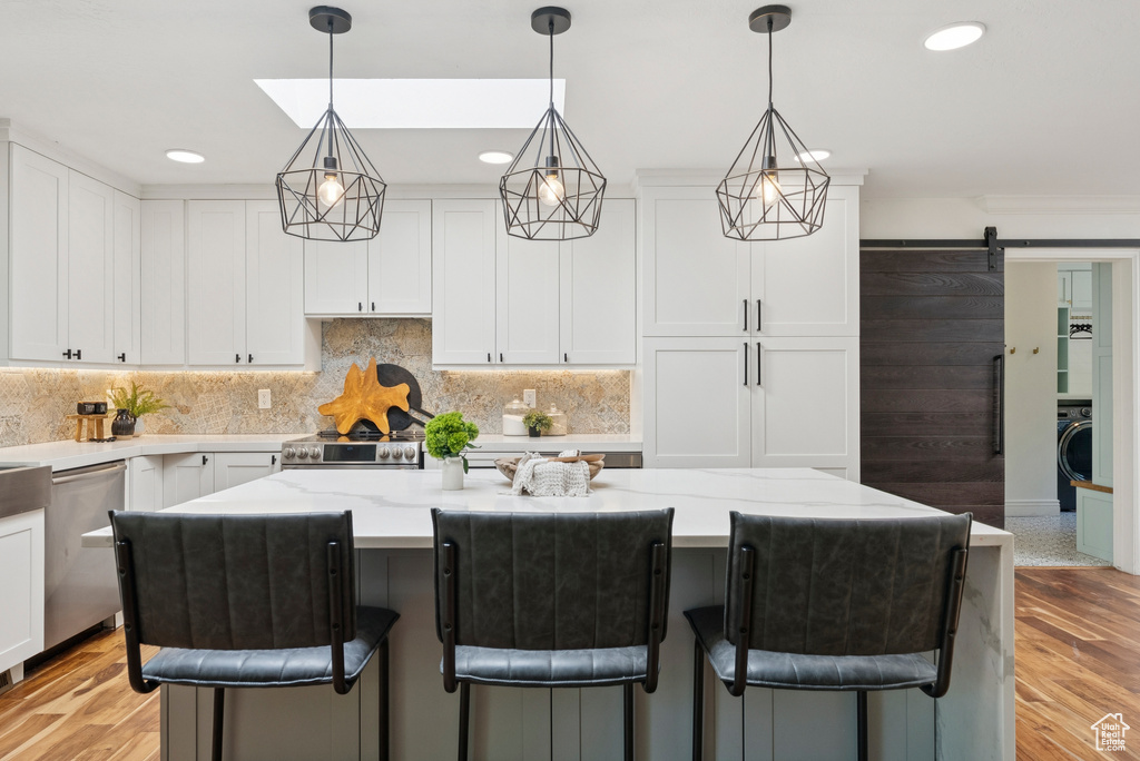 Kitchen featuring stainless steel appliances, washer / dryer, white cabinetry, a barn door, and light wood-style floors