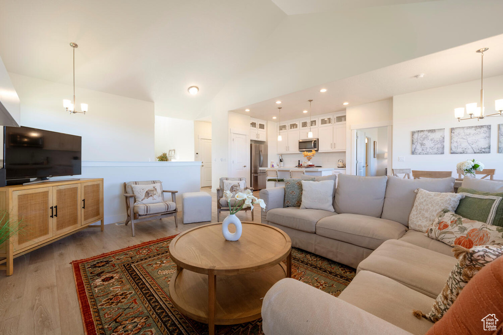 Living room featuring a notable chandelier, light wood-type flooring, and vaulted ceiling