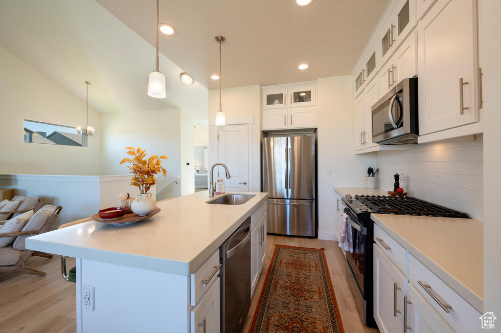 Kitchen featuring white cabinets, sink, a kitchen island with sink, decorative light fixtures, and stainless steel appliances