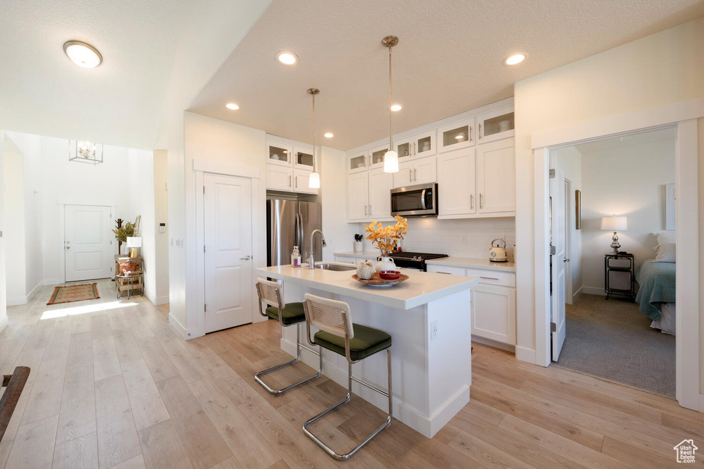 Kitchen with appliances with stainless steel finishes, light hardwood / wood-style floors, white cabinetry, a center island with sink, and sink