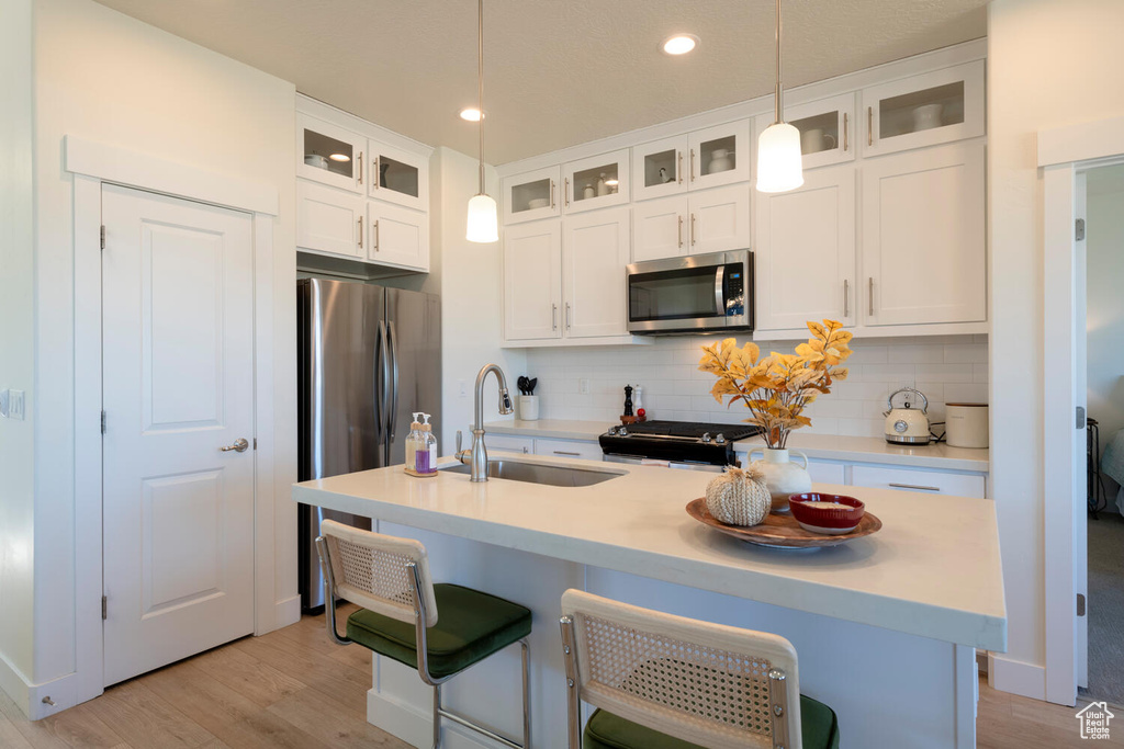 Kitchen with appliances with stainless steel finishes, decorative backsplash, pendant lighting, light wood-type flooring, and sink