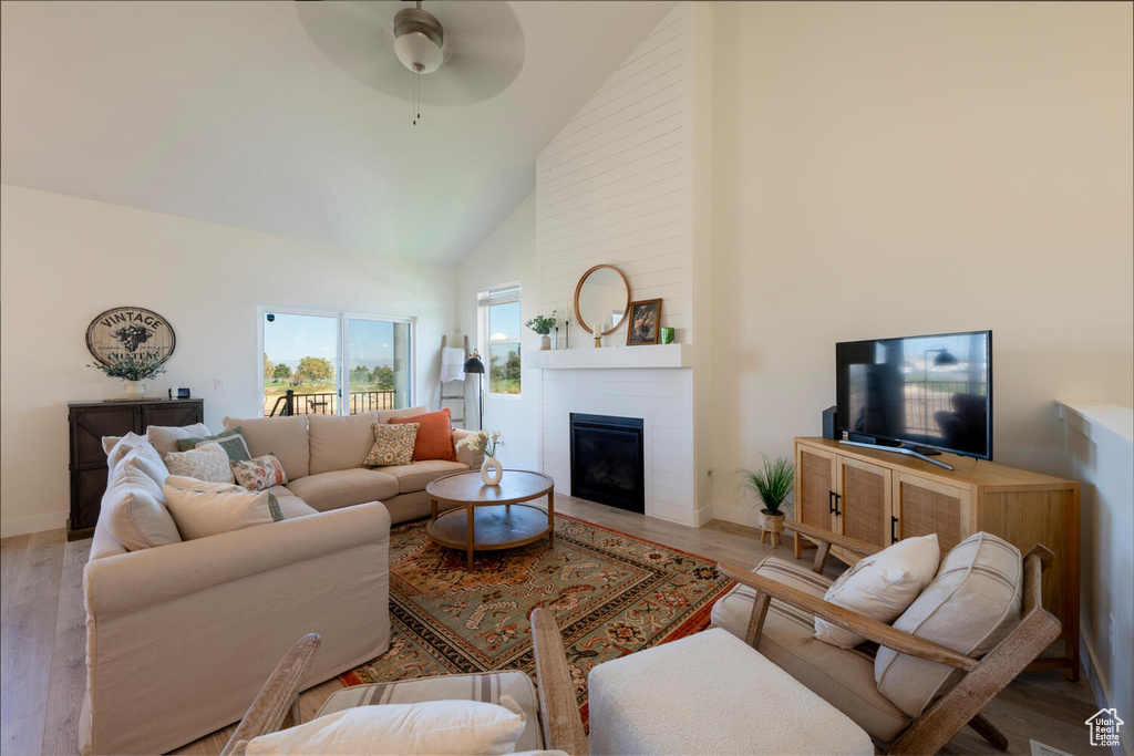 Living room with ceiling fan, light wood-type flooring, high vaulted ceiling, and a large fireplace