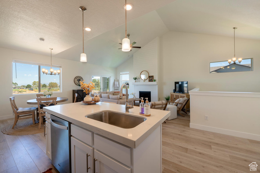 Kitchen featuring ceiling fan with notable chandelier, a fireplace, light hardwood / wood-style flooring, stainless steel dishwasher, and sink