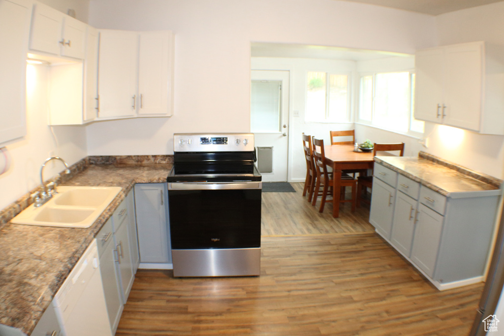 Kitchen with electric range, sink, white cabinets, hardwood / wood-style floors, and white dishwasher