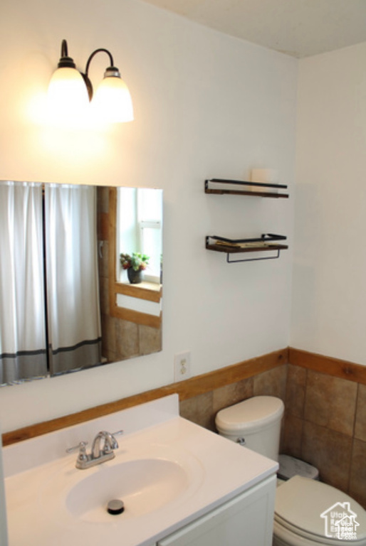 Bathroom featuring vanity, tile walls, and toilet