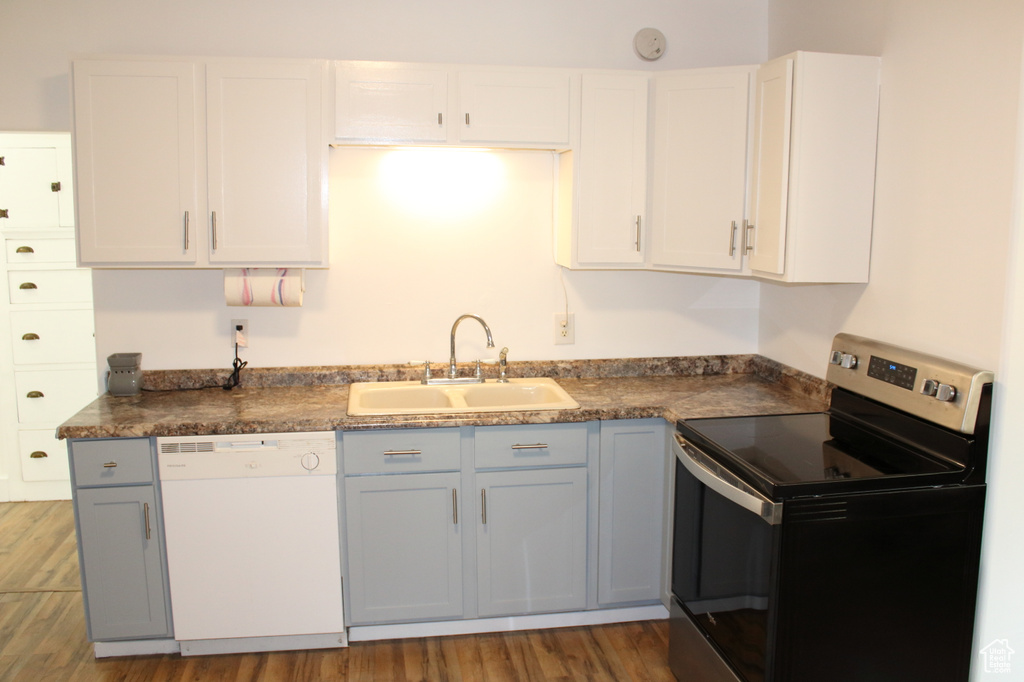 Kitchen featuring wood-type flooring, sink, white cabinetry, stainless steel range with electric stovetop, and white dishwasher