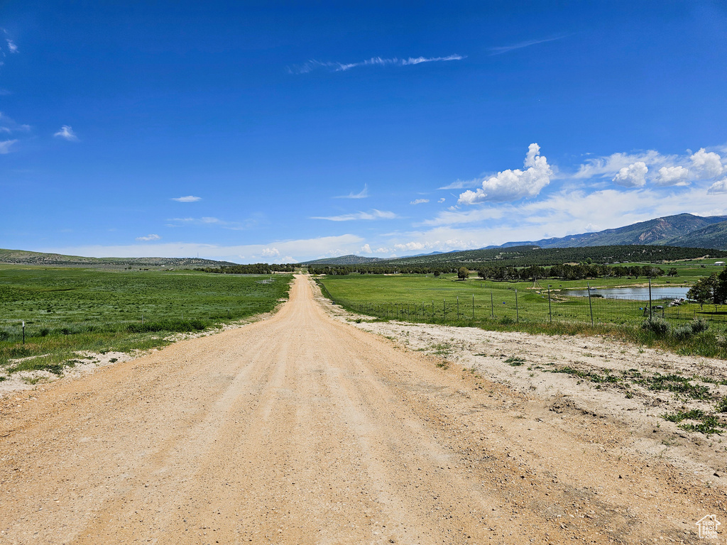 View of dirt / gravel road with a water and mountain view and a view of rural / pastoral area