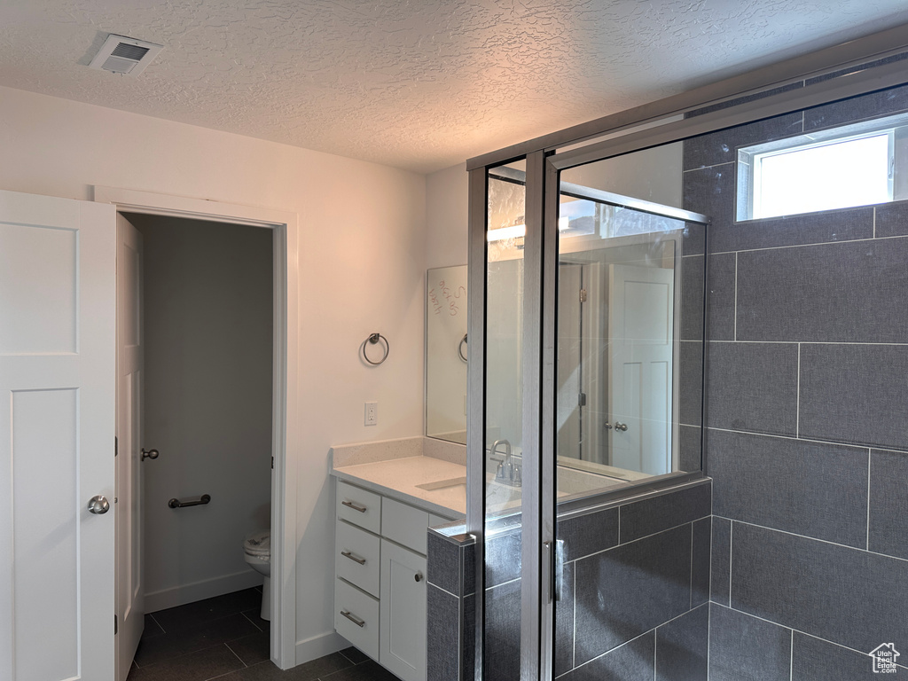 Bathroom with toilet, tile patterned floors, a shower with door, vanity, and a textured ceiling