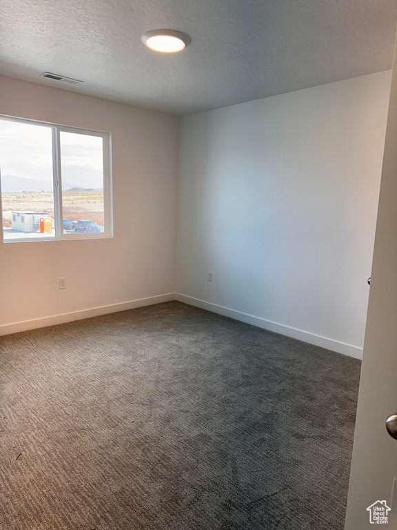 Empty room with dark carpet and a textured ceiling