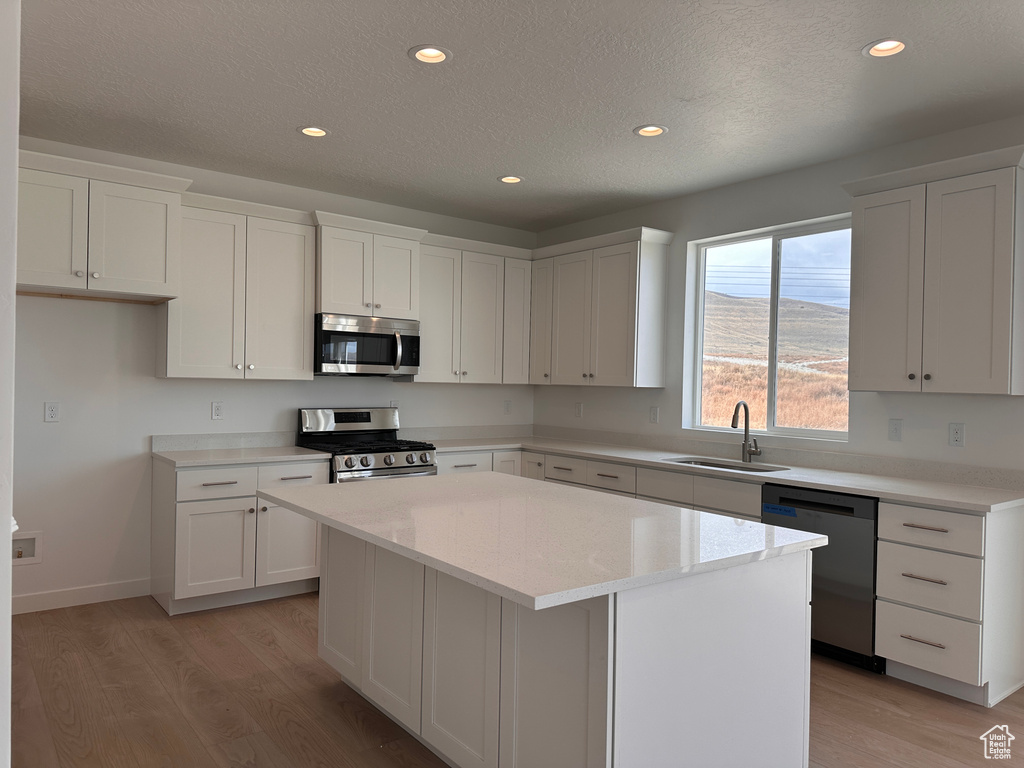 Kitchen with a kitchen island, stainless steel appliances, white cabinets, sink, and light hardwood / wood-style flooring