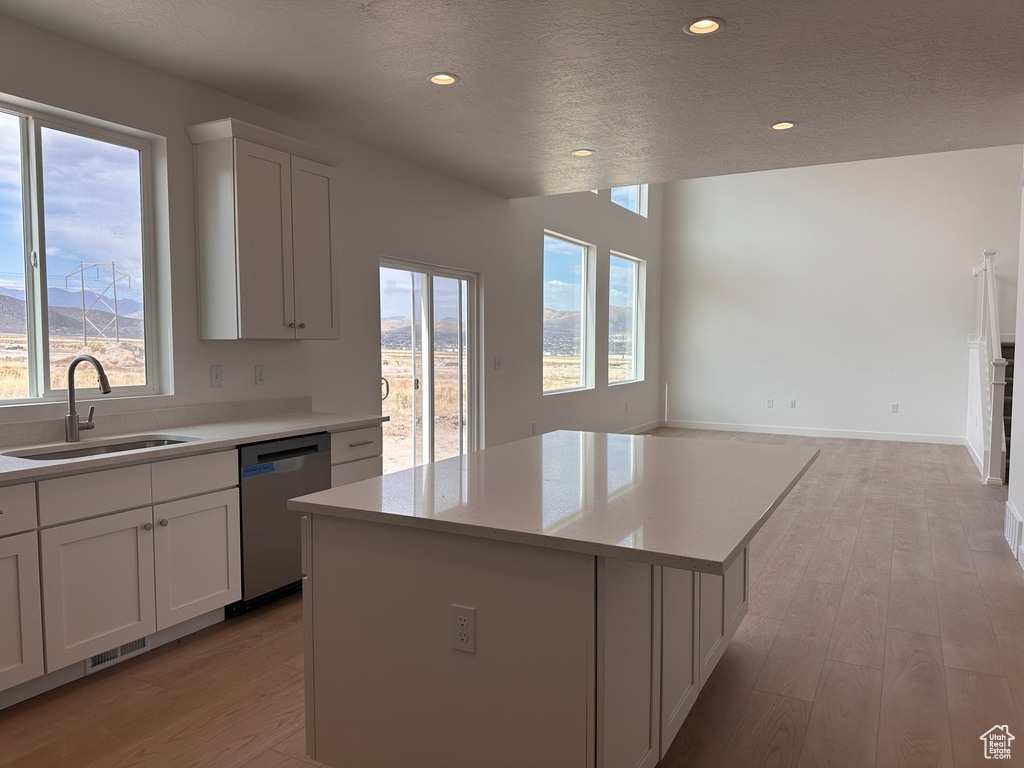 Kitchen featuring dishwasher, white cabinetry, a center island, and a healthy amount of sunlight