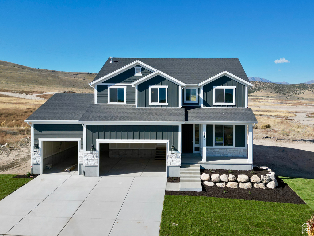 View of front of house with a garage, a porch, a front lawn, and a mountain view