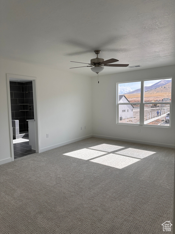 Carpeted empty room featuring ceiling fan, a mountain view, and a textured ceiling