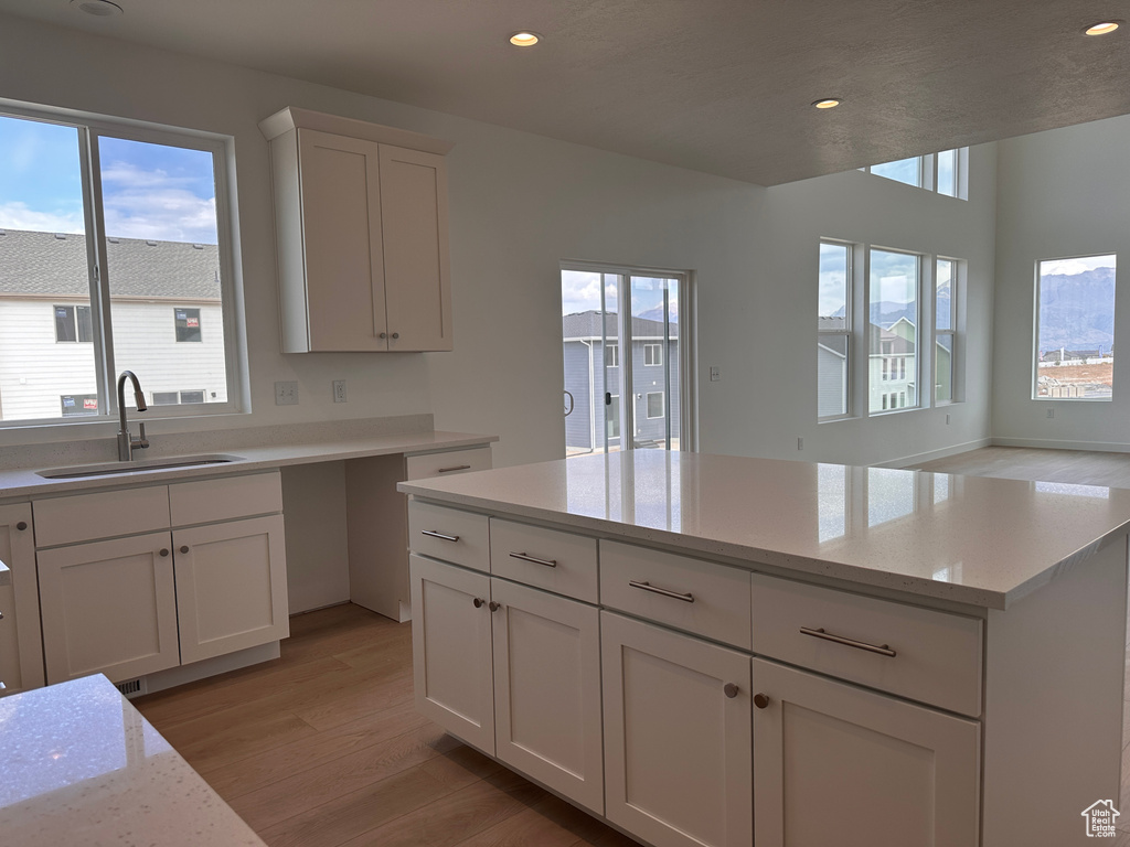 Kitchen with light stone countertops, light hardwood / wood-style flooring, white cabinets, and sink