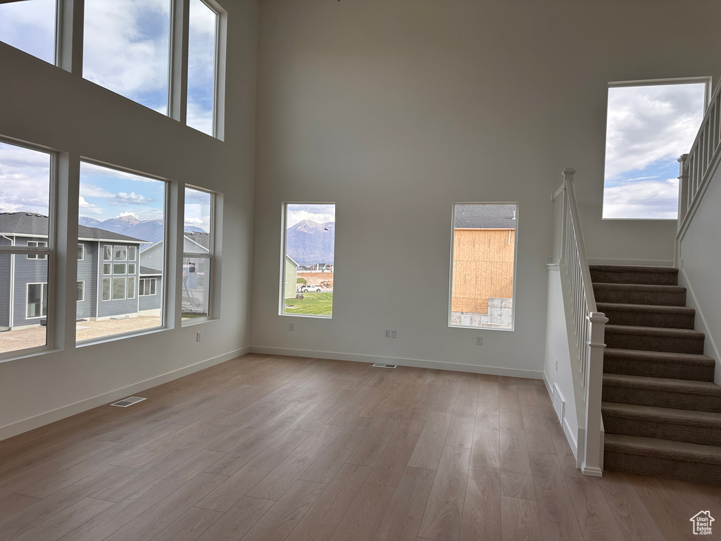 Unfurnished living room featuring light hardwood / wood-style flooring, a high ceiling, and a wealth of natural light