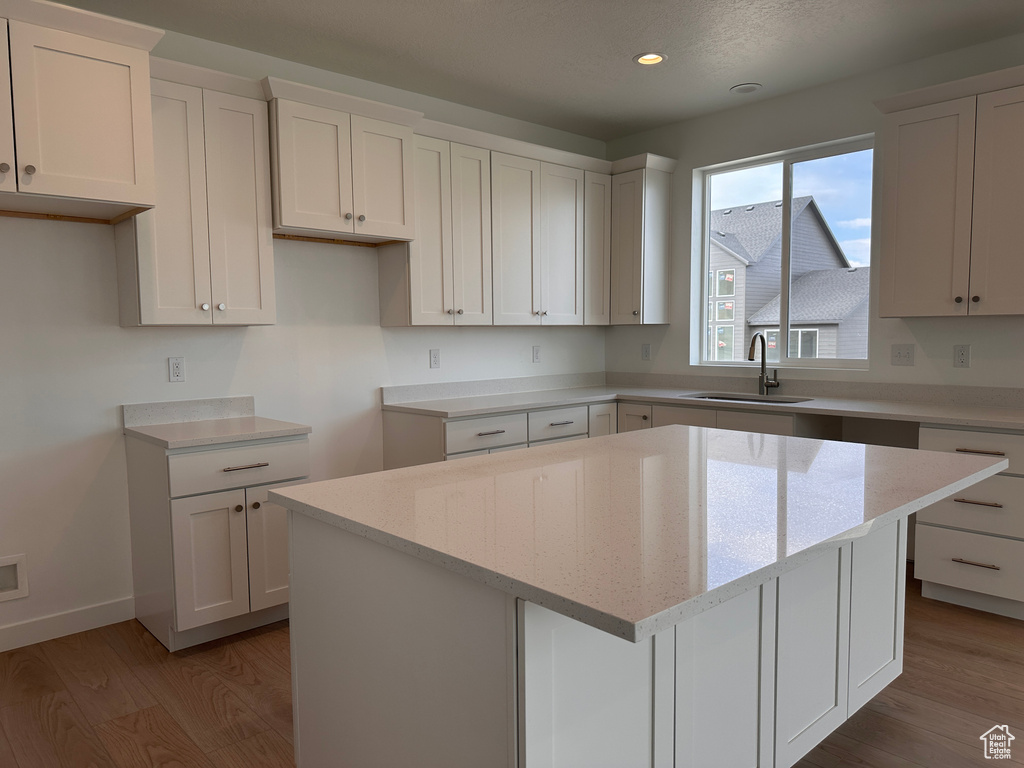 Kitchen with white cabinets, light stone countertops, sink, a kitchen island, and light wood-type flooring