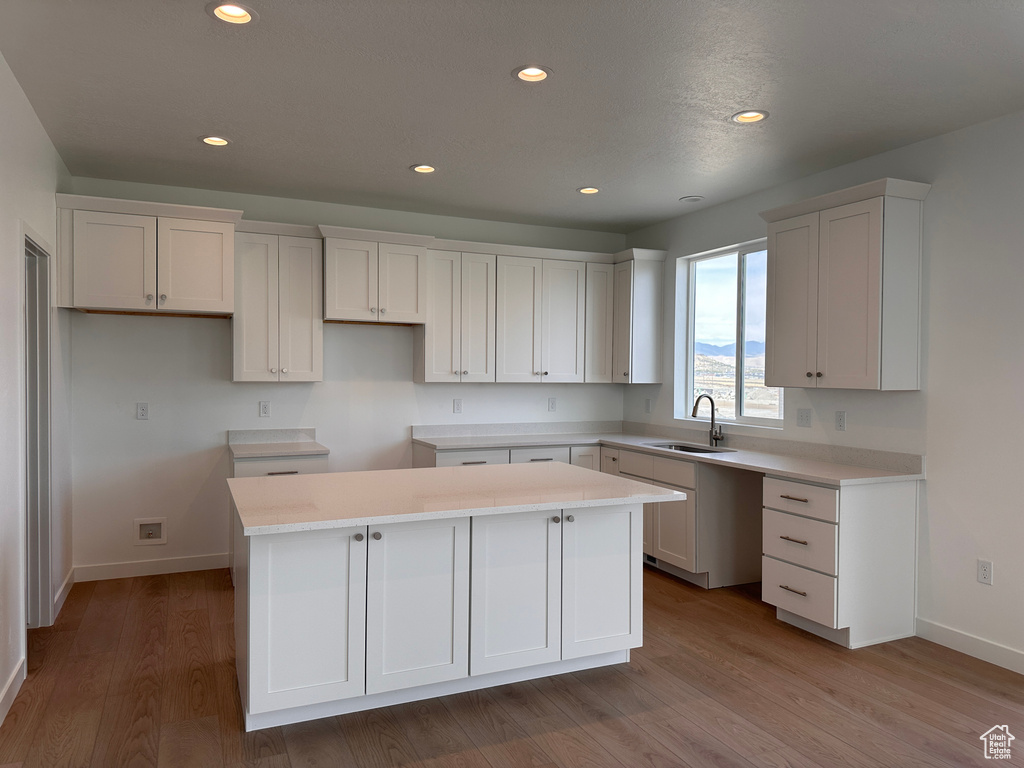 Kitchen with sink, light hardwood / wood-style floors, white cabinetry, and a kitchen island