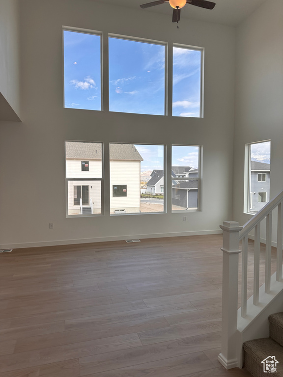 Unfurnished living room featuring ceiling fan, plenty of natural light, light hardwood / wood-style floors, and a towering ceiling