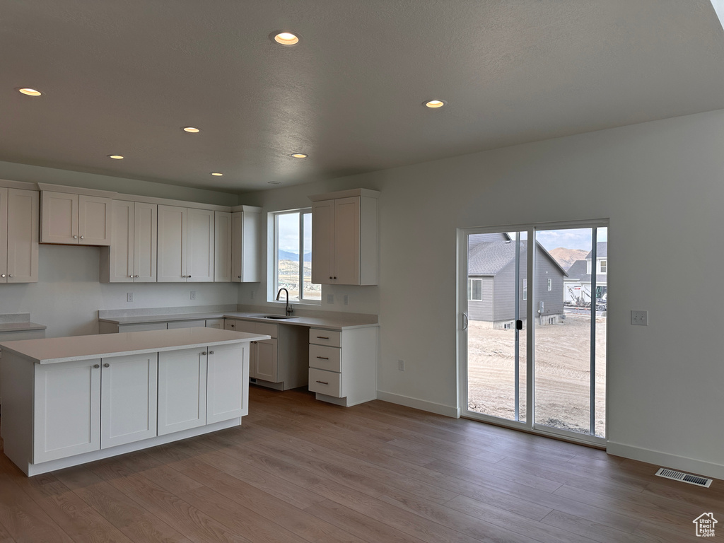 Kitchen featuring white cabinets, sink, light hardwood / wood-style floors, and a center island