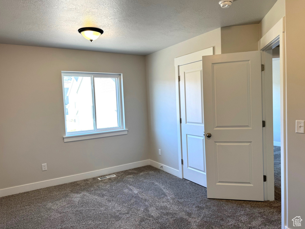 Unfurnished bedroom featuring a textured ceiling and dark colored carpet