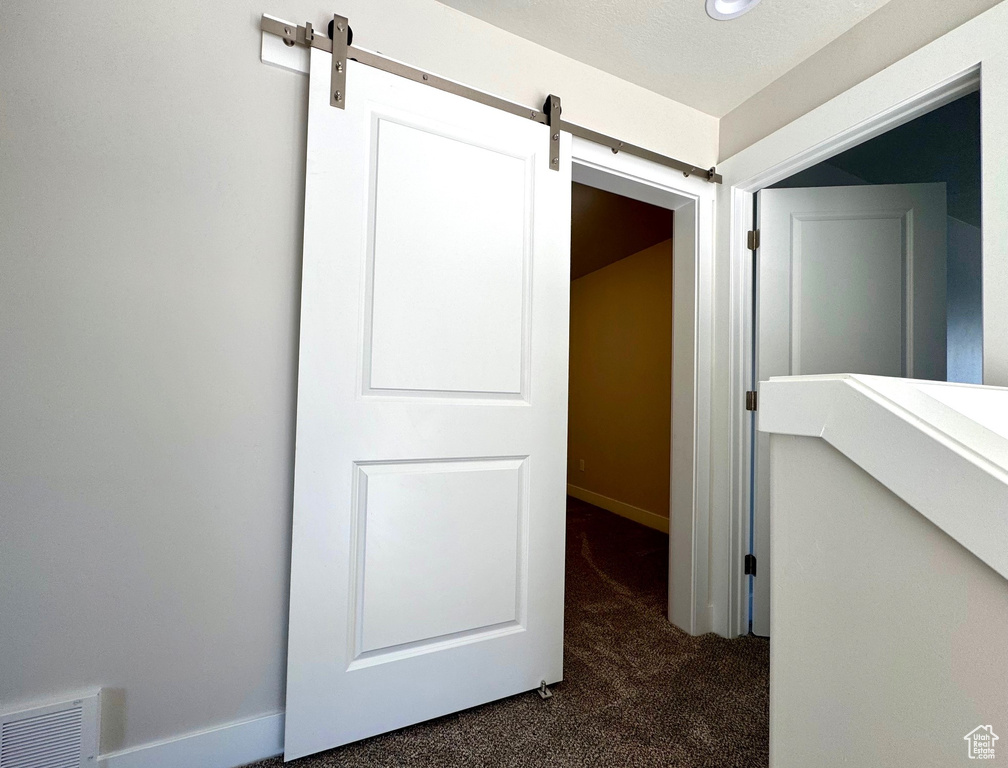 Corridor with a barn door, a textured ceiling, and dark colored carpet