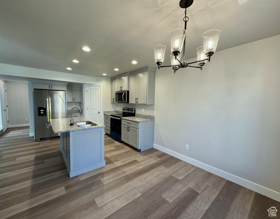 Kitchen with sink, a center island with sink, appliances with stainless steel finishes, a notable chandelier, and light stone countertops