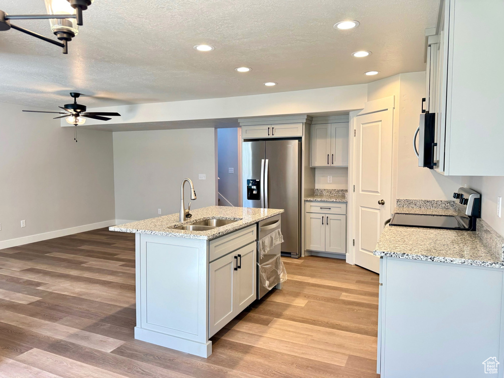 Kitchen with ceiling fan, sink, a kitchen island with sink, stainless steel appliances, and light hardwood / wood-style floors