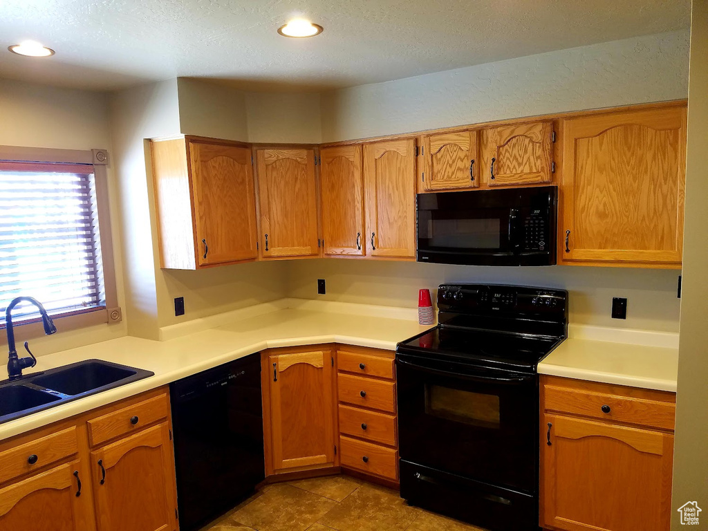 Kitchen featuring a textured ceiling, black appliances, sink, and light tile patterned floors