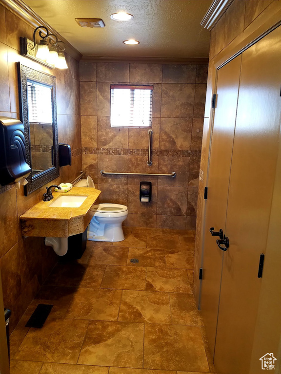 Bathroom featuring a textured ceiling, tile walls, sink, and toilet