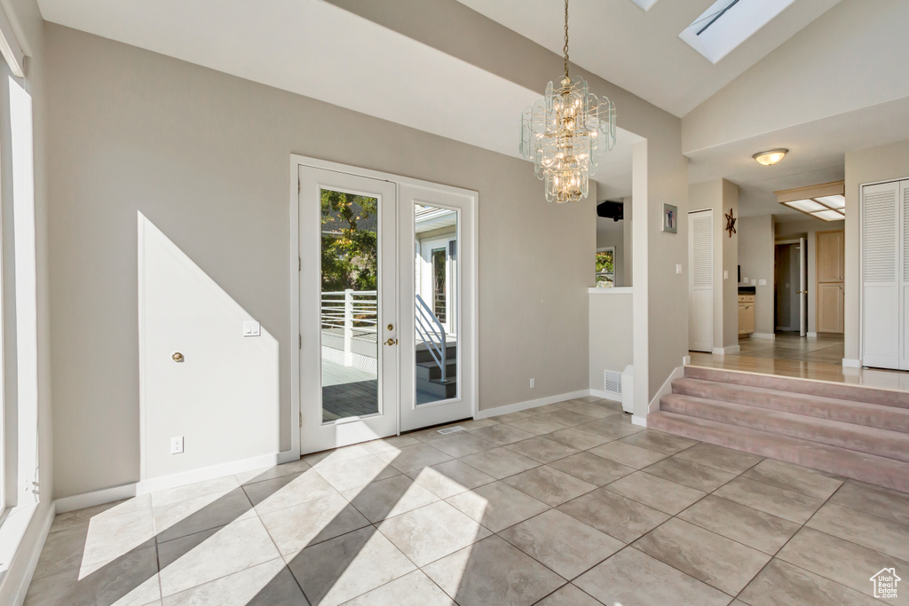 Tiled spare room with vaulted ceiling with skylight and an inviting chandelier