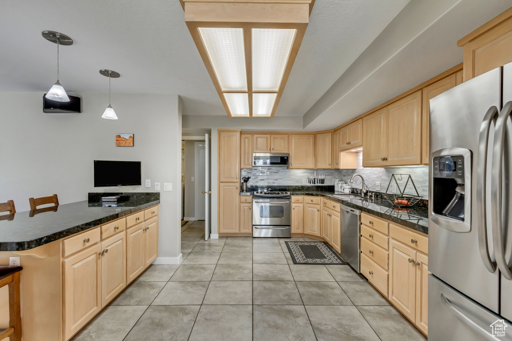 Kitchen featuring light brown cabinets, kitchen peninsula, decorative light fixtures, stainless steel appliances, and a kitchen breakfast bar