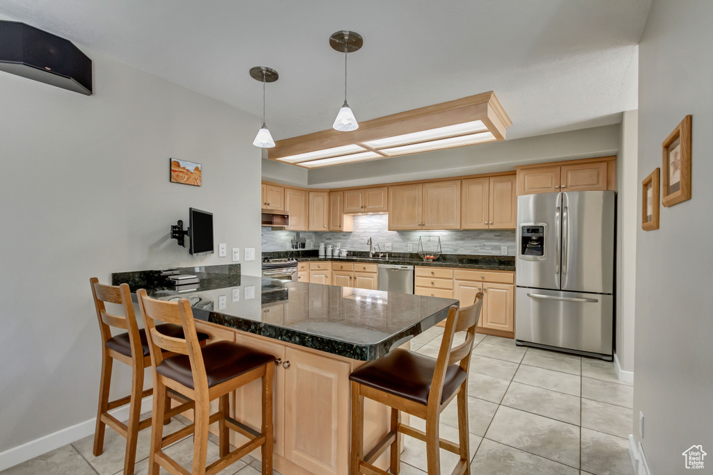 Kitchen with appliances with stainless steel finishes, decorative backsplash, kitchen peninsula, light brown cabinets, and a kitchen bar