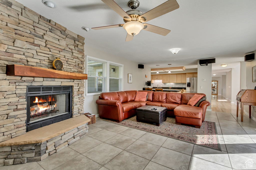 Living room featuring light tile patterned floors, a stone fireplace, and ceiling fan