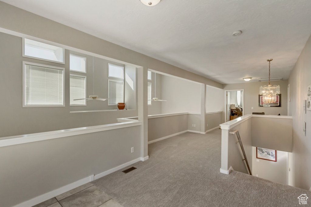 Corridor featuring light colored carpet and an inviting chandelier