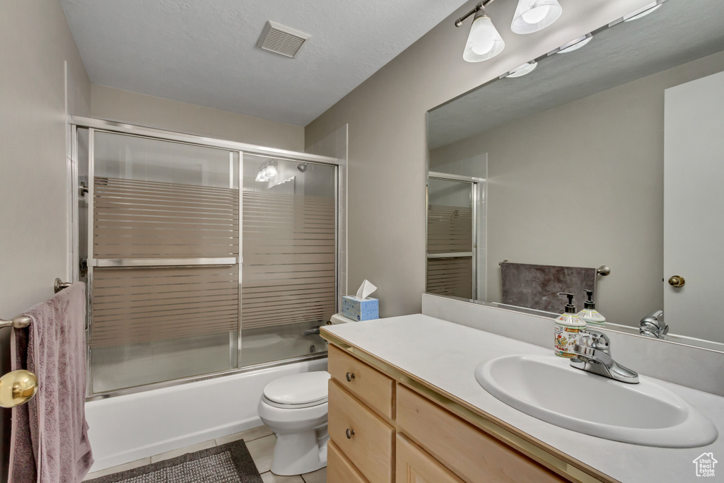 Full bathroom featuring tile patterned floors, toilet, vanity, and bath / shower combo with glass door