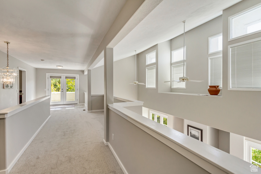 Hallway featuring an inviting chandelier, light colored carpet, and french doors