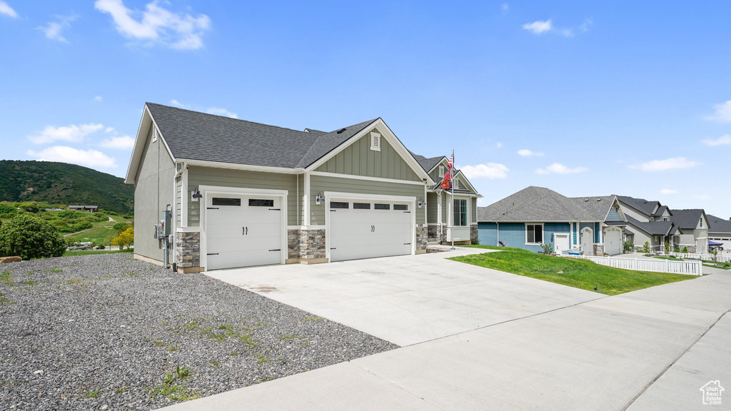 Craftsman-style home featuring an attached garage, board and batten siding, concrete driveway, stone siding, and roof with shingles