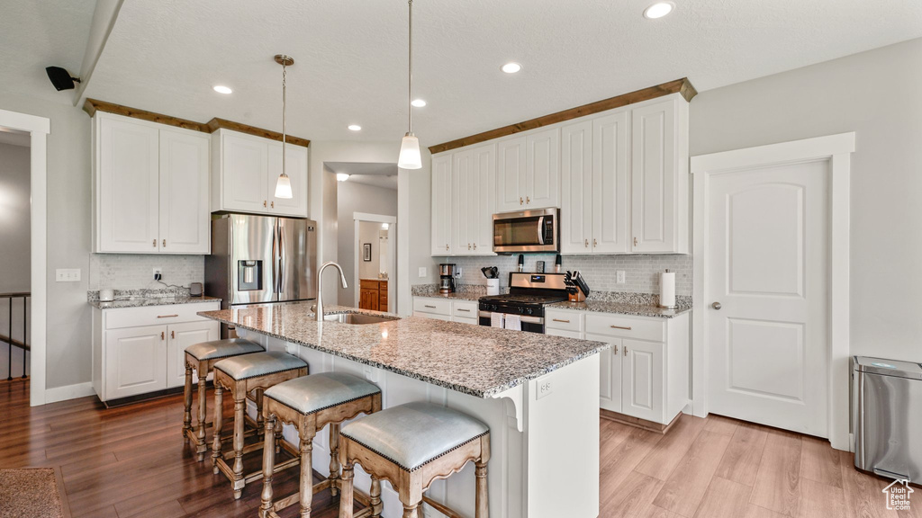 Kitchen with appliances with stainless steel finishes, a sink, light wood-style flooring, tasteful backsplash, and recessed lighting