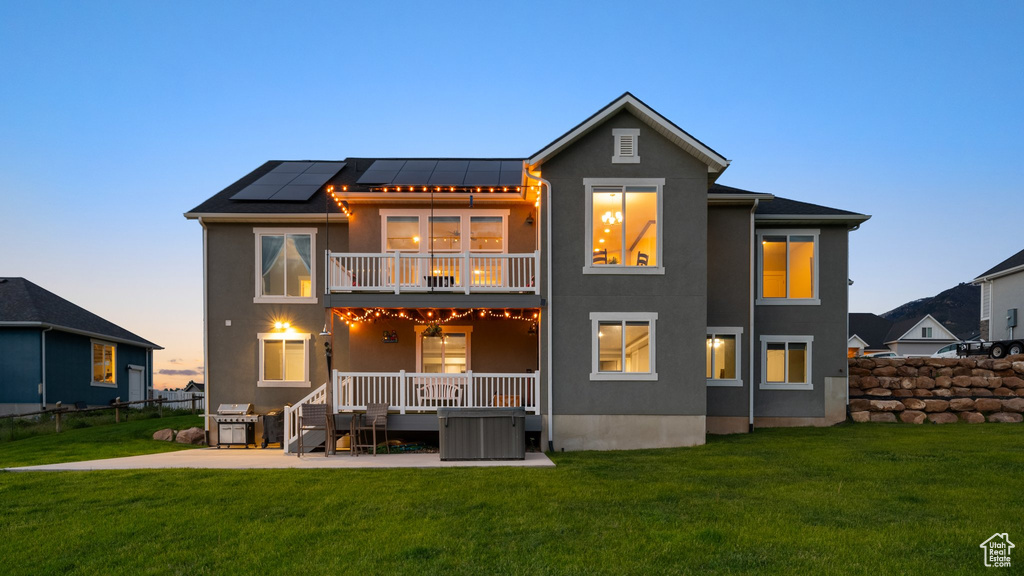 Back of house at dusk featuring a balcony, roof mounted solar panels, stucco siding, a patio area, and a standing seam roof