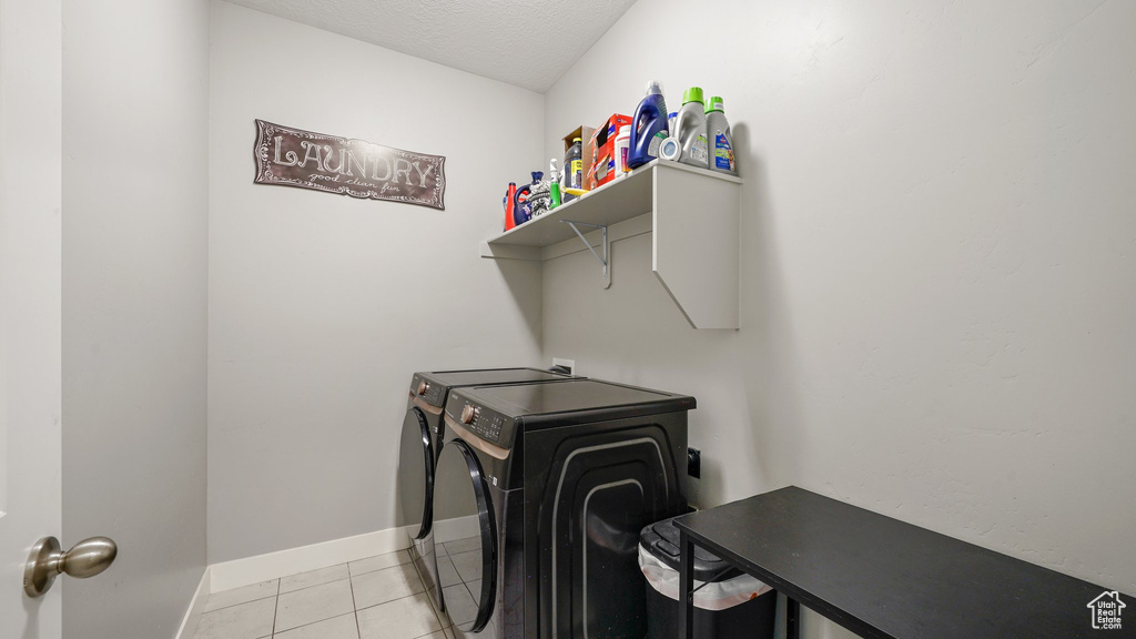 Laundry area with washing machine and dryer, baseboards, light tile patterned flooring, and a textured ceiling