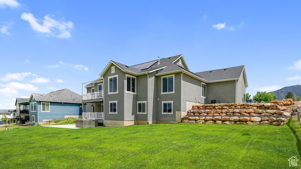 Back of house featuring roof mounted solar panels, a balcony, a yard, stucco siding, and cooling unit