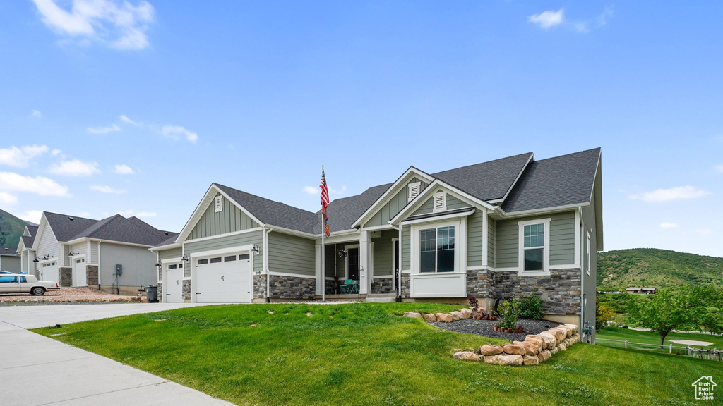 Craftsman house featuring board and batten siding, stone siding, a front yard, and concrete driveway