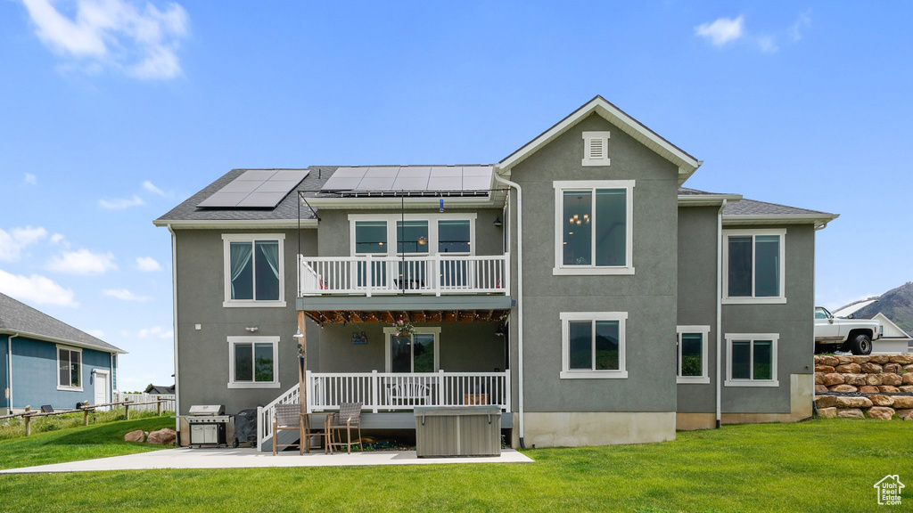 Rear view of house featuring stucco siding, solar panels, a balcony, and a patio area