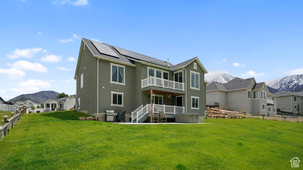 Rear view of property with a balcony, roof mounted solar panels, a mountain view, a jacuzzi, and stucco siding