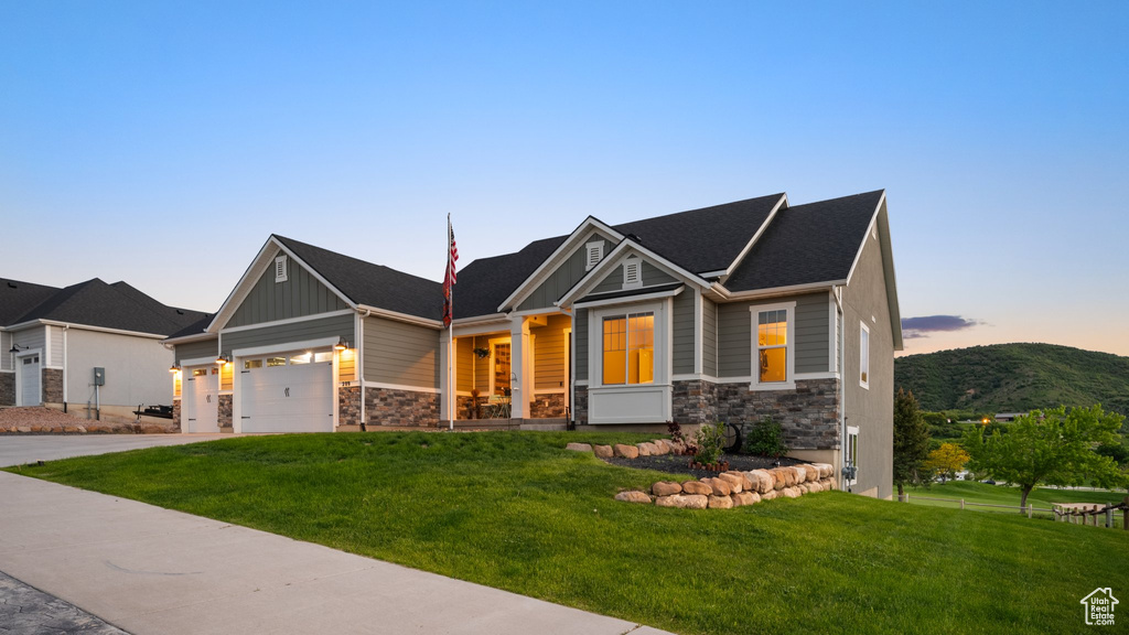 Craftsman house featuring stone siding, a front yard, a garage, and driveway
