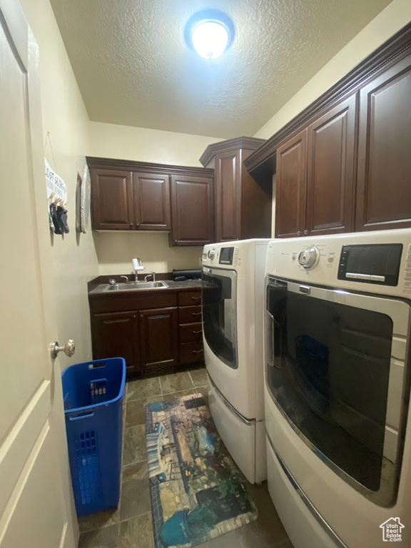 Laundry area with cabinets, a textured ceiling, washer and dryer, and sink