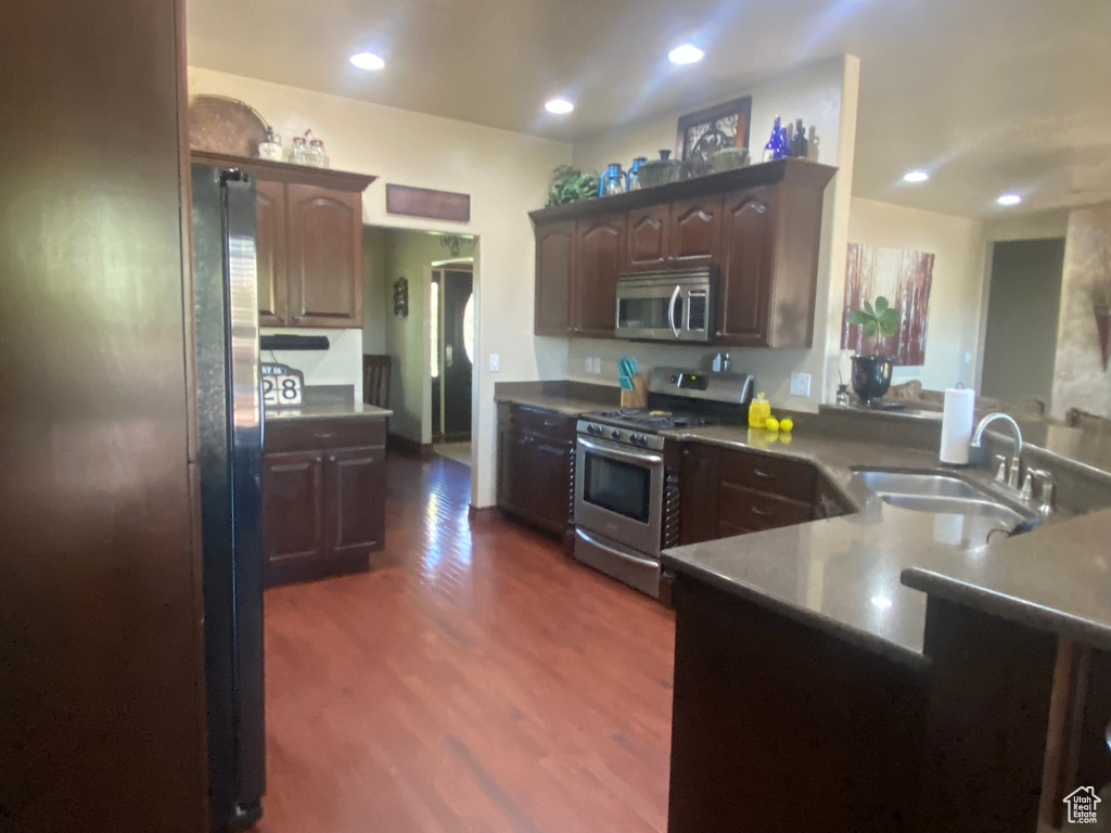 Kitchen featuring dark brown cabinetry, kitchen peninsula, sink, stainless steel appliances, and dark hardwood / wood-style flooring