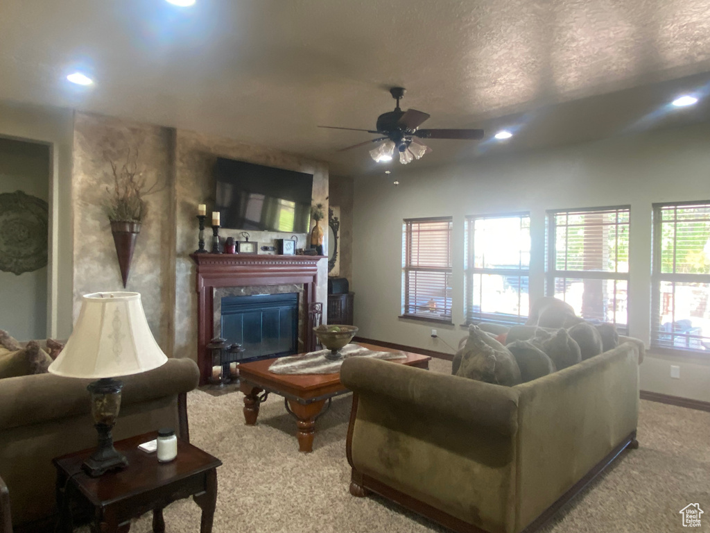 Living room with ceiling fan, a high end fireplace, light colored carpet, and a wealth of natural light