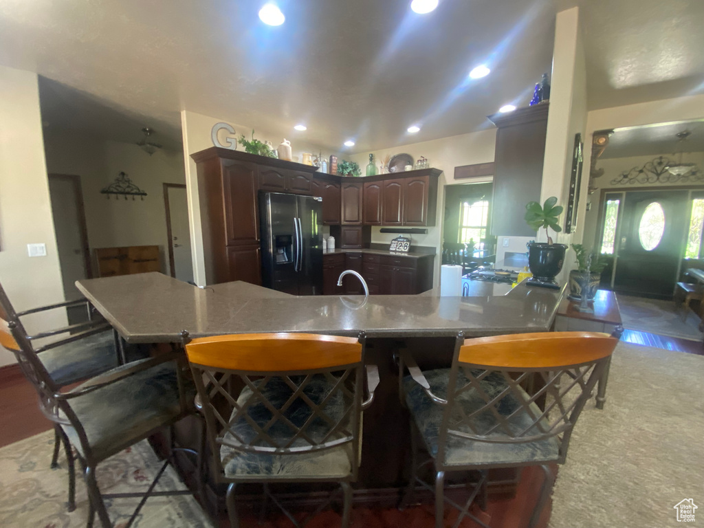 Kitchen with a kitchen breakfast bar, stainless steel refrigerator with ice dispenser, kitchen peninsula, and dark brown cabinetry