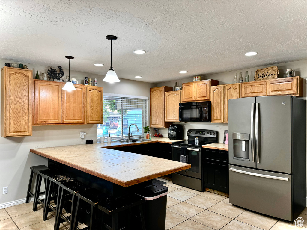 Kitchen featuring a textured ceiling, black appliances, light tile patterned flooring, and sink